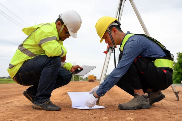 Asian surveyor engineer two people checking level of soil with Surveyor\'s Telescope equipment to measure leveling for cut and fill, started leveling the ground at the highway road construction site.