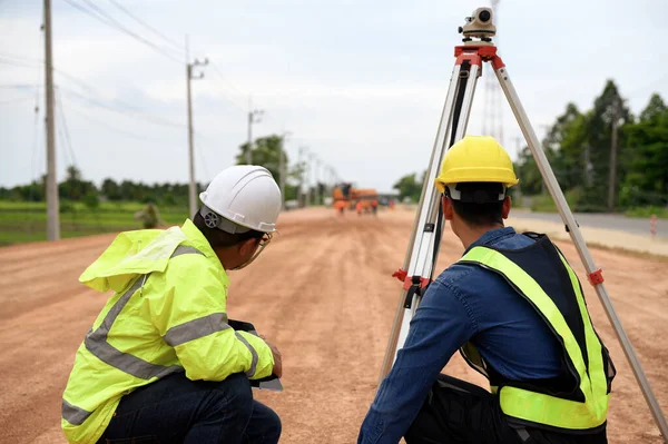 Asian surveyor engineer two people checking level of soil with Surveyor\'s Telescope equipment to measure leveling for cut and fill, started leveling the ground at the highway road construction site.