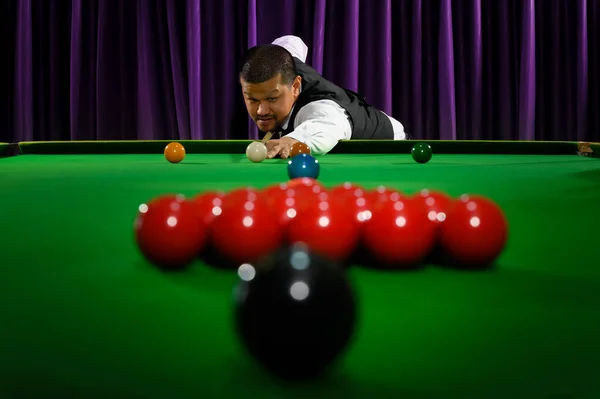 アジアのスヌーカープレーヤーの肖像画は スヌーカーテーブルでゲームにセットされた赤いボールグループを打つために白いボールシュートを目指しています — ストック写真