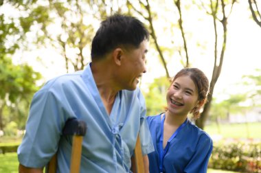 Asyalı Kadın Doktor Kıdemli Hastaya Yardım Ediyor ve Tedavi sırasında Teşvik Ediyor. Koltuk değneği olan Asyalı Emekli Hastaların Rehabilitasyon veya Fiziksel Terapisi.