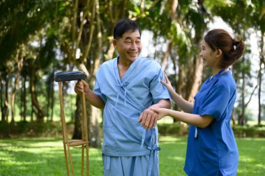 Asyalı Kadın Doktor Kıdemli Hastaya Yardım Ediyor ve Tedavi sırasında Teşvik Ediyor. Koltuk değneği olan Asyalı Emekli Hastaların Rehabilitasyon veya Fiziksel Terapisi.