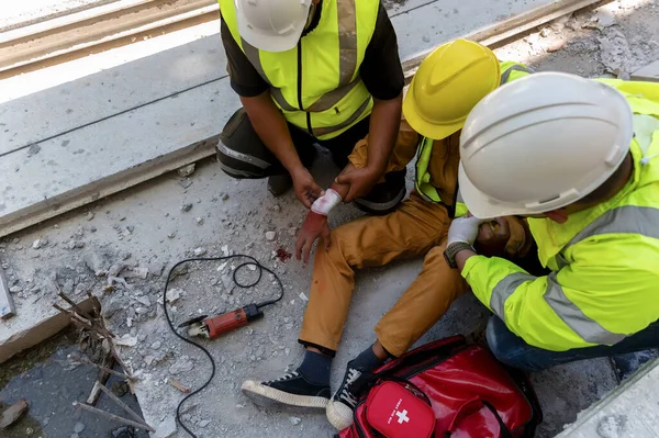 First aid team support to builder worker after hand injury bleeding, accident at work, Using construction power tools unsafe and negligence at the construction site. Safety in work concept.