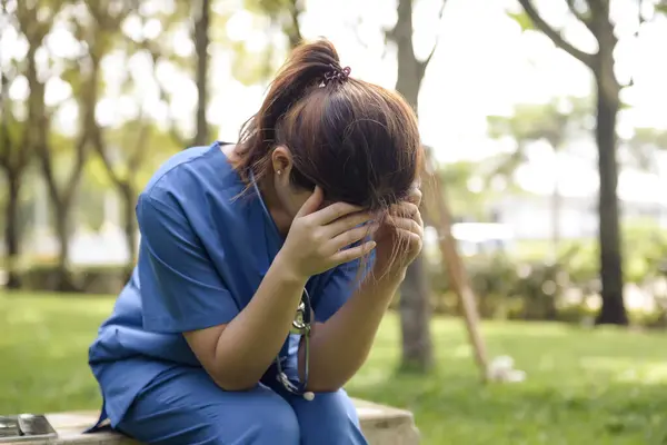 Asian Female Doctor Sitting Stressed in the Middle of a Green Garden, Working Stress and Headache with Many Difficult Cases.