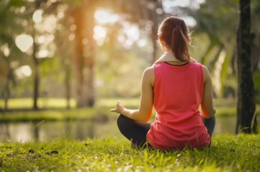 Genç kadınlar halka açık parkta sıcak akşam ışığında egzersiz yaptıktan sonra çimenlerde oturup yoga çalışırlar..