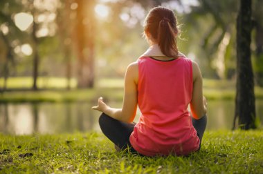 Genç kadınlar halka açık parkta sıcak akşam ışığında egzersiz yaptıktan sonra çimenlerde oturup yoga çalışırlar..