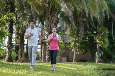 Asyalı Yaşlı Baba ve Kızı yeşil bir parkta koşuyor ve dinleniyor, temiz havayı soluyor ve güzel manzaranın tadını çıkarıyorlar. Sağlık ve aile bağı.