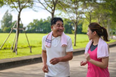 Asyalı Yaşlı Baba ve Kızı yeşil bir parkta koşuyor ve dinleniyor, temiz havayı soluyor ve güzel manzaranın tadını çıkarıyorlar. Sağlık ve aile bağı.