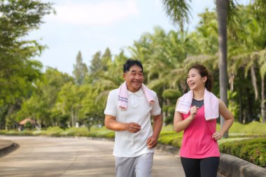 Asyalı Yaşlı Baba ve Kızı yeşil bir parkta koşuyor ve dinleniyor, temiz havayı soluyor ve güzel manzaranın tadını çıkarıyorlar. Sağlık ve aile bağı.