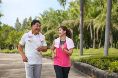 Asyalı Yaşlı Baba ve Kızı yeşil bir parkta koşuyor ve dinleniyor, temiz havayı soluyor ve güzel manzaranın tadını çıkarıyorlar. Sağlık ve aile bağı.