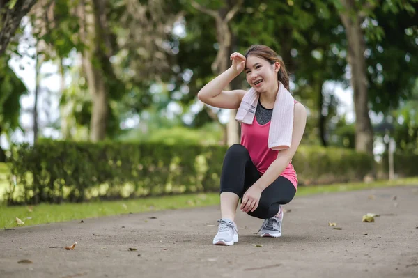 An Asian Woman Is break from jogging With A Gentle Smile In The Park Is Full Of Trees. Looks Around The Park and Smiles While Feels Happy And Alive