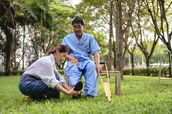 Daughter takes care to foot massage her father, Encourage him during his illness in hospital garden. The happiness of old adult patients while rehabilitation or physical therapy of retired patients.