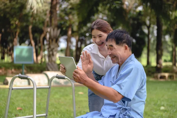 Daughter helps her father who is recovering at the hospital. in using communication technology tablets. Communicate with family members in the hospital\'s park.