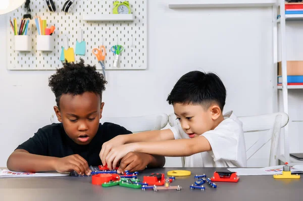 Two Children of different ethnicities are playing together to learn about electrical circuits basics on the table in homeschool classrooms. Brainstorming ideas and sharing their knowledge.