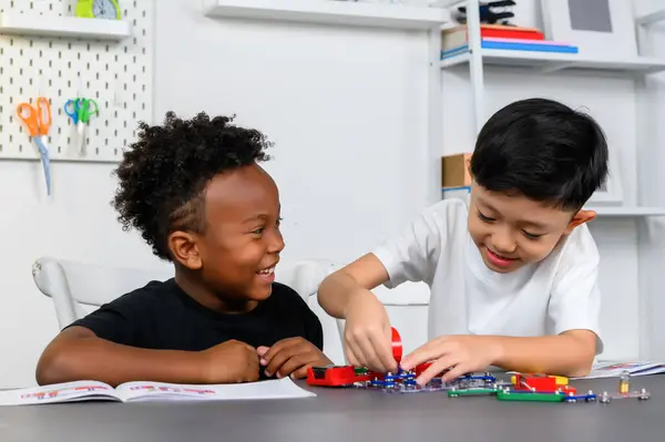 Two Children of different ethnicities are playing together and enjoy learning about electrical circuits basics on table in a homeschool classroom. Brainstorming ideas and sharing their knowledge.