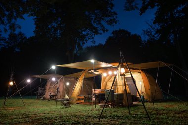 Açık hava kamp çadırı çimen avlusunda ve karanlık mavi gökyüzü altında sıcak gece ışığı alacakaranlık zamanı, tatilde aile pikniği tatilde dinlenme, aile turistlerinin kamp manzarası..