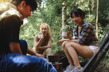 Genç İnsanlar Seyahat Grubu Yağmur Ormanlarında Oturuyor ve Kamp Sobası ile Su Kaynatıyor. Kahve ve su içme kampı. Yolculukta Gruplar İçin Kolay Kamp Yemekleri Hazırlayın.