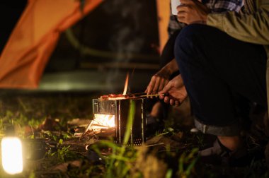 Sırt çantalı grubun vahşi ortamında ızgara ızgarasına yakın çekim. Yürüyüş grupları için ızgara yemekler, doğada kamp yapmak, sıcak ve davetkar bir atmosferle gece yemek pişirmek..