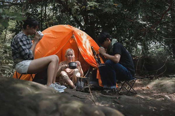 Young People Trekking Group Sitting Relaxed in the Rainforest and Boil Water with a Camp Stove. Campsite Drinking Coffee and Water on Trekking Trips.