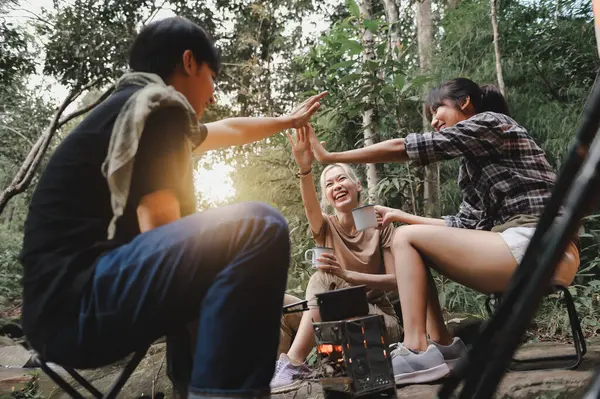Young People Trekking Group Sitting Relaxed and Team Giving High Five in the Rainforest while Boil Water with a Camp Stove, Campsite Drinking Coffee and Water on Trekking Trips.