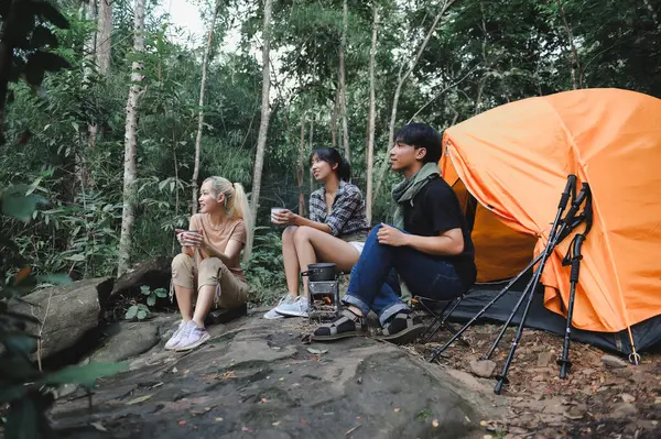 Young People Trekking Group Sitting Relaxed in the Rainforest and Boil Water with a Camp Stove. Campsite Drinking Coffee and Water. Prepare Easy Camping Meals for Groups on Trekking Trips.