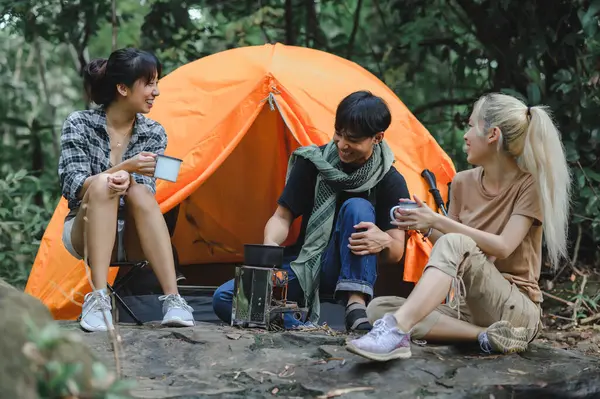 Young People Trekking Group Sitting Relaxed Talk in the Rainforest and Boil Water with a Camp Stove. Campsite Drinking Coffee and Water on Trekking Trips.