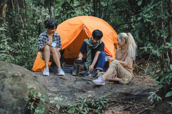Young People Trekking Group Sitting Relaxed Talk in the Rainforest and Boil Water with a Camp Stove. Campsite Drinking Coffee and Water on Trekking Trips.