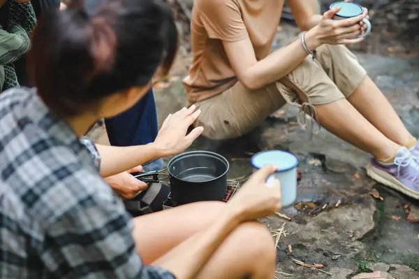 People Trekking Group Boil Water and Check Water Temperature by Hand while Holding the Cup. Boil Water for Clean and Hygiene in the Forest. Campsite Drinking Coffee and Clean Water on Trekking Trips.