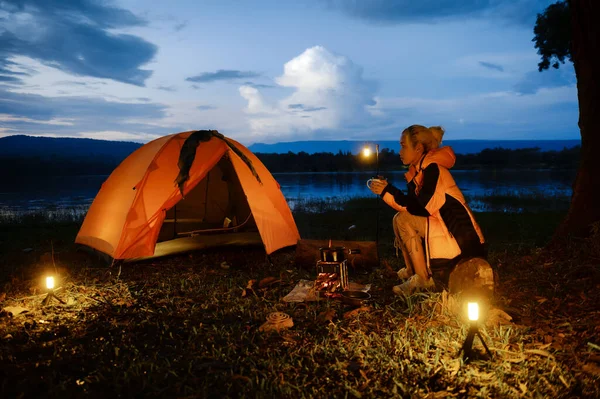 Female traveler or Backpacker sits by the camping stove near her tent, Enjoying the atmosphere of surrounding nature, Relaxation beneath the blue sky while waiting for boiling water prepares cooking.