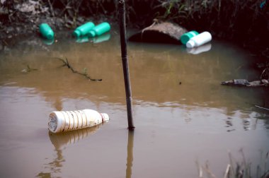 Doğal su kaynağında kimyasal dolu çöp şişeleri var. Su kirliliği kavramı.
