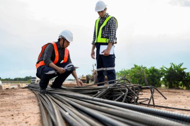 İnşaat mühendisleri, yol inşaatlarında hammadde teftişi ve beton takviyesi yaparken güvenlik kaskı takıyorlar. Araştırmacı ve beton yapı yapısını kontrol ediyor.