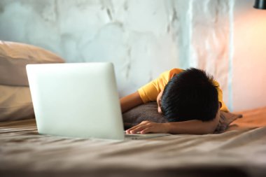 Asyalı çocuk yorgun düşene kadar dizüstü bilgisayarda uzanıp sosyal medyayı izliyor ve elektronik cihazların yanında uyuyakalıyor. Çevrimdışı rahatlama kavramı için sosyal medya dijital detoks.