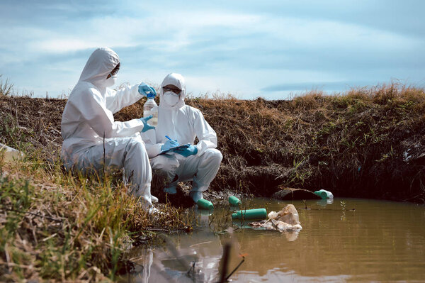 Team of scientists or biologists wears protective clothing to collect water samples from a natural water source with chemical-filled bottles of trash. Water pollution concept.