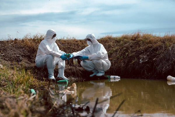 Team of scientists or biologists wears protective clothing to inspect chemical-filled bottles of trash on the natural water source and note. Water pollution concept.