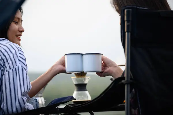 Asian young woman two persons sitting cheers coffee cup together and enjoying coffee drink outdoors in the morning time, Coffee drink relaxing on the morning summer camping vacation.