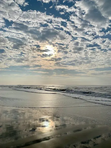Sahilde gün doğumunun fotoğrafı, dalgalı açık deniz, bulutlar arasında güneş.