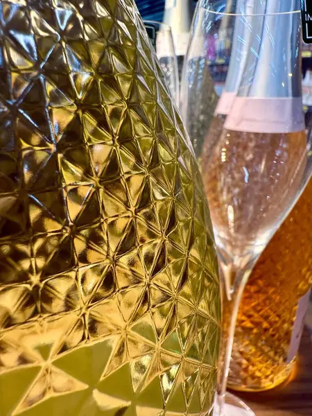 Ananas kabuğu desenli ve arka planda bir bardak olan güzel, köpüklü şarap şişeleri. 
