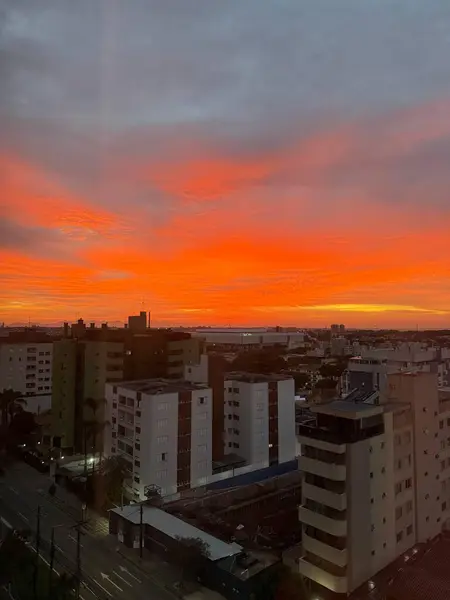 Canlı turuncu günbatımı hareketli bir şehir silueti üzerine sıcak bir ışık saçıyor, gökdelenler renkli gökyüzüne karşı siluetlenmiş ve sokaklar modern mimariyle dolu..