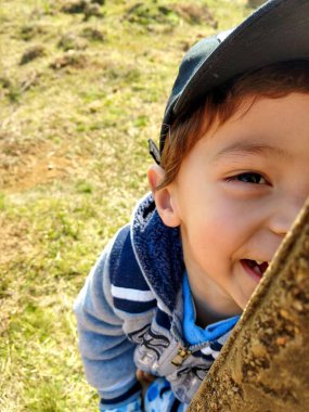 Güneşli bir kış günü kırsal kesimde keşfedildiğinde, altı yaşlarında bir çocuk bir kep takıyor ve sırıkla gülümsüyor..