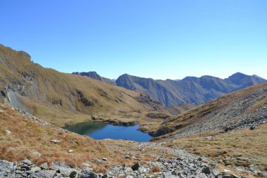 Resim, Romanya 'nın Fgra Dağları' na kurulmuş Capra Gölü 'nü gösteriyor. Sivri tepeler ve kayalık arazilerle çevrili, kristal berrak dağlık göl engebeli güzelliği yansıtıyor..
