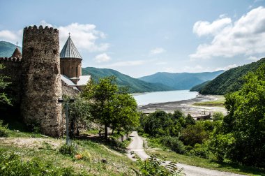 Bu fotoğrafta, Gürcistan 'ın yemyeşil tepelerine kurulmuş çarpıcı Ananuri Kalesi yer alıyor. Tarihi taş kuleleri ve kubbeli kilisesi, doğa ve tarih manzarası sunan parlak mavi bir gökyüzü tarafından çerçevelenmiştir.