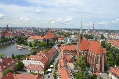 Wroclaw 'ın bu hava manzarası, ikonik kırmızı çatılı binalar, görkemli bir Gotik kilise ve şehir manzarasında dolanan kanalların yer aldığı tarihi cazibesini sergiliyor. Tarih ve modern şehir hayatının mükemmel bir karışımı..