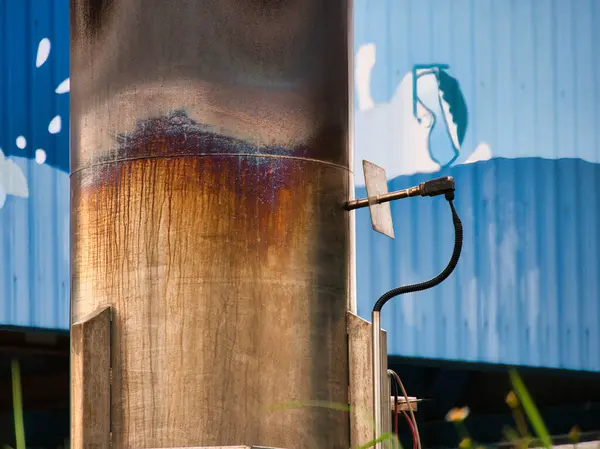 Üzerinde küçük bir vana ve hortum bulunan paslı endüstriyel boru, açık mavi boyalı bir duvara yaslanmış, deniz atı desenli, metal ve boya desenleri görünür..