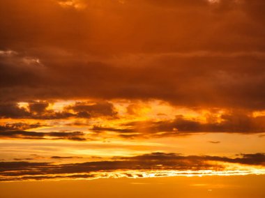 Kıyı şeridi üzerinde canlı bir günbatımı. Uzakta rüzgar türbinlerinin koyu siluetleri ve turuncu, pembe ve mor renklerle boyanmış renkli bir gökyüzü..