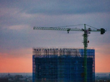 Alacakaranlıkta mavi-gri gökyüzüne karşı inşaat vincinin üzerinde iniş ışıkları olan bir uçak..