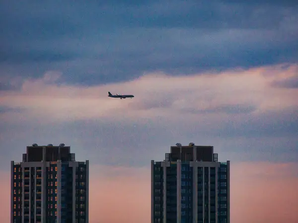Gün batımında yumuşak, renkli gökyüzünde iki yüksek bina arasında bir uçak süzülür..