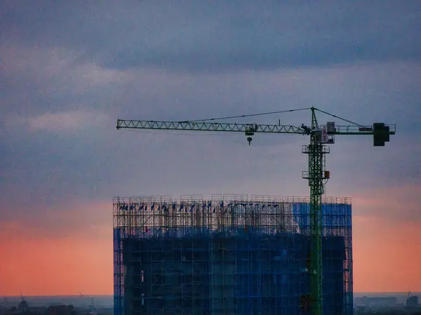 Alacakaranlıkta mavi-gri gökyüzüne karşı inşaat vincinin üzerinde iniş ışıkları olan bir uçak..