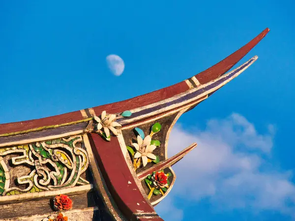 Renkli, dekoratif bir çatı üzerinde, parlak mavi bir gökyüzünde yarım ay yükselir. Karmaşık çiçek oymalarıyla..