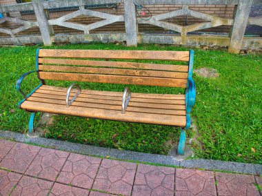 Metal kolları ve bisiklet kilitleri olan eskimiş ahşap bir bank kaldırım yollarının yanındaki çimlere oturur..