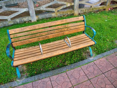 Metal kolları ve bisiklet kilitleri olan eskimiş ahşap bir bank kaldırım yollarının yanındaki çimlere oturur..