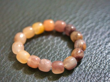 Renkli boncuklu bir bilezik, çeşitli gölgelerde yuvarlak pürüzsüz boncuklar, desenli bir yüzeye yerleştirilmiş..